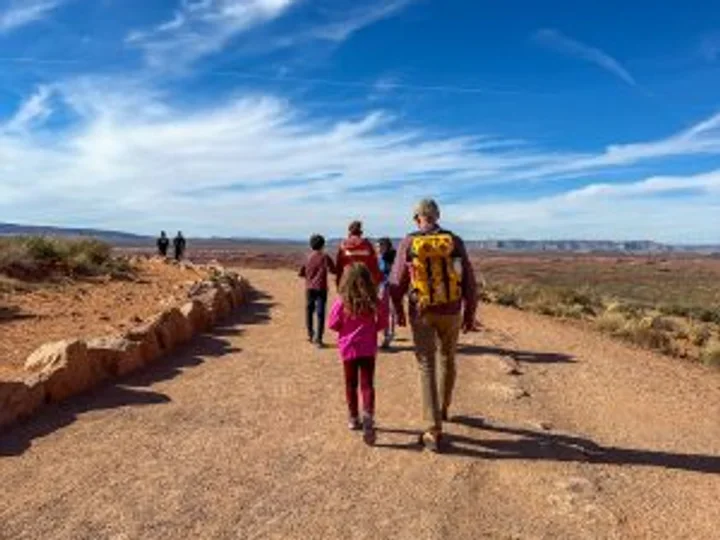 Hikers walking the hard-packed sand trail toward Horseshoe Bend overlook under a blue sky