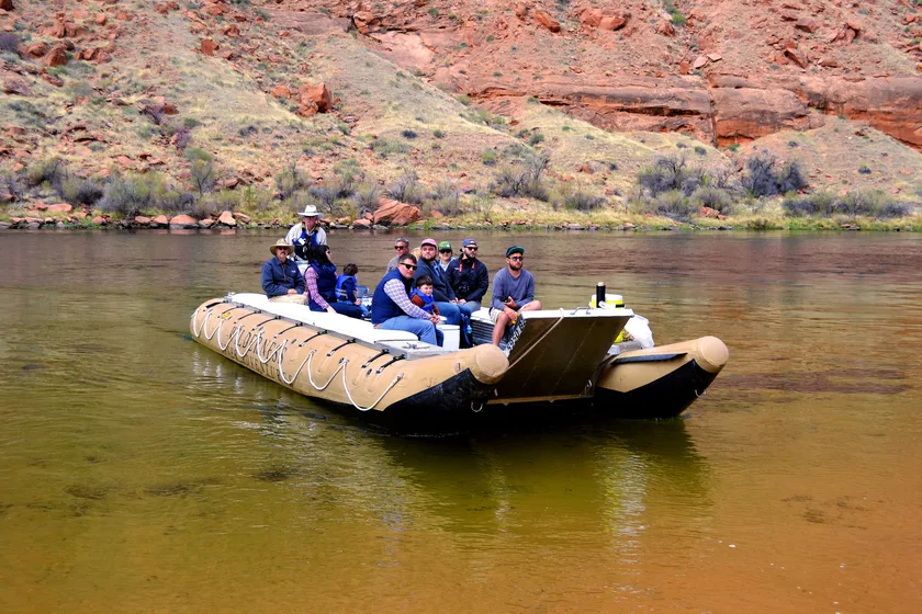 Group of visitors on a pontoon raft floating the Colorado River through red canyon walls
