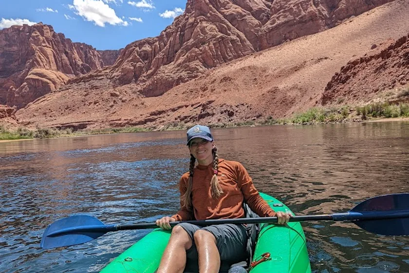 Kayaker on a green kayak on the Colorado River with dramatic red sandstone cliffs behind
