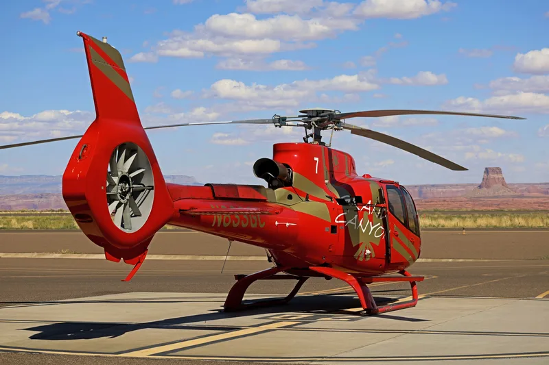 Red EcoStar helicopter on the tarmac at Page Municipal Airport with canyon mesas behind