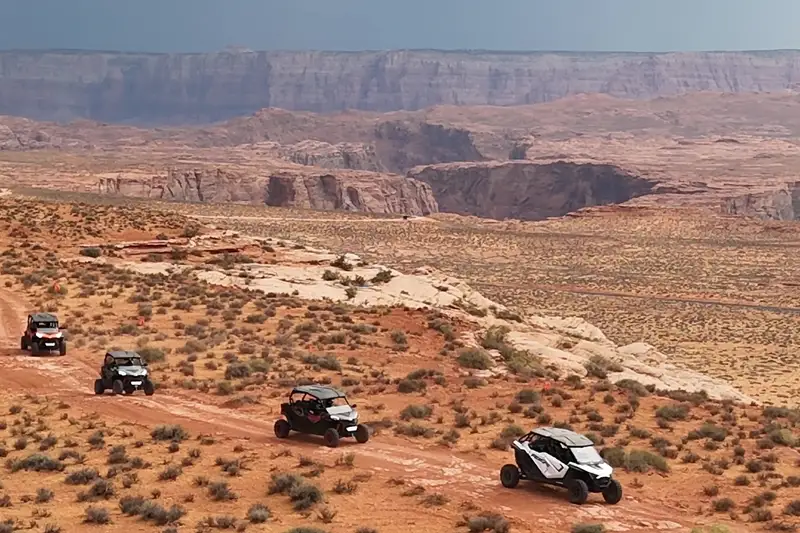 Line of UTVs driving a red-dirt desert trail toward the canyon rim near Horseshoe Bend